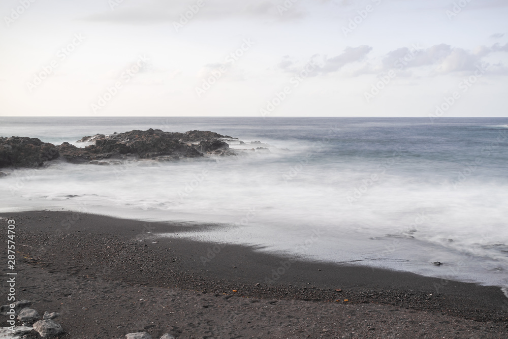 Mesa del mar volcanic beach sand and rocks, long exposure photography, with Atlantic ocean waves, horizon with sunset light, Tacoronte, Tenerife, Canary islands, Spain Mesa del mar volcanic beach sand and rocks, long exposure photography, with Atlantic ocean waves, horizon with sunset light, Tacoronte, Tenerife, Canary islands, Spain