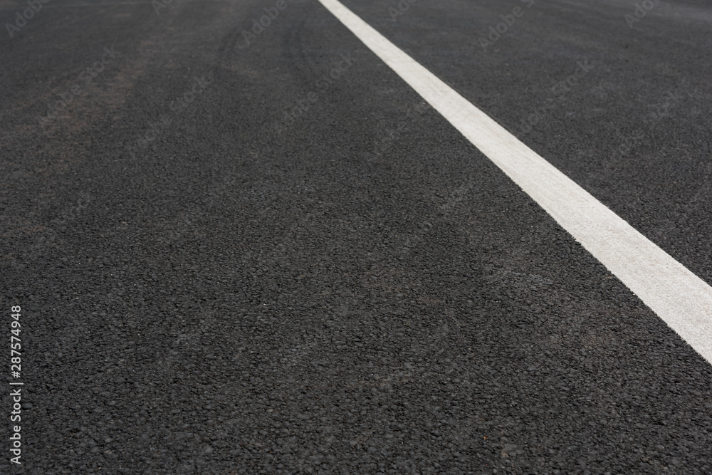 Low angle view of a white paint slash on black asphalt road