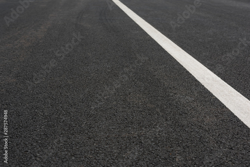 Low angle view of a white paint slash on black asphalt road © bqmeng