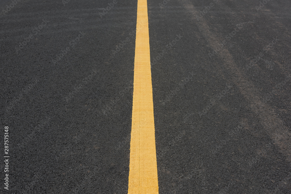 A straight yellow paint line in the middle of an asphalt road