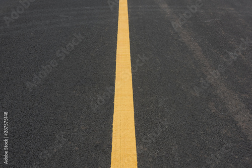 A straight yellow paint line in the middle of an asphalt road © bqmeng