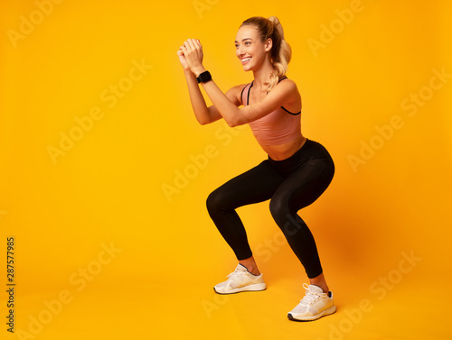 Foto Millennial Girl Doing Deep Squat Exercise On Yellow Background