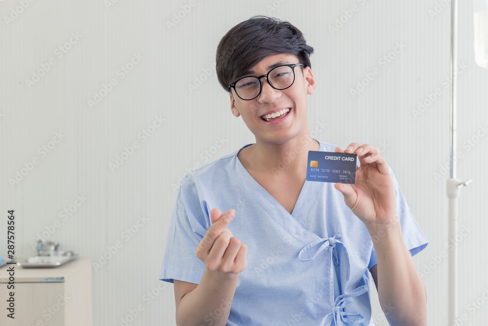 Young teenage Asian man holding credit card sitting on the bed in the hospital. Young teenage Asian man holding credit card sitting on the bed in the hospital.