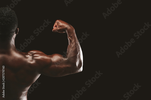 Strong biceps of afro bodybuilder on black background