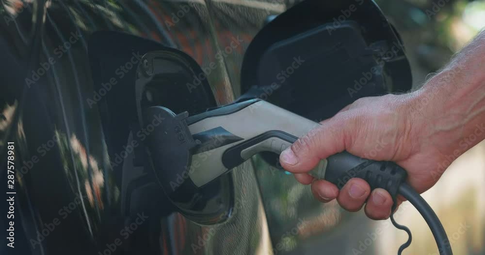 Slow motion close up of power supply plugged into an electric car for charging a modern battery which is the future of the automobile and new era of vehicle fuel on the street.