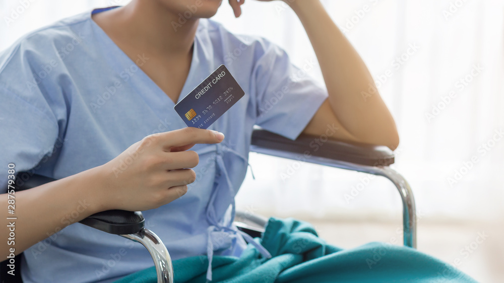 Young teenage Asian man holding credit card sitting on the bed in the hospital with smiley face. healthcare and medical concept.