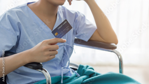 Young teenage Asian man holding credit card sitting on the bed in the hospital with smiley face. healthcare and medical concept.