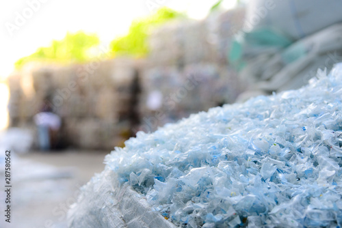 Close up PET plastic bottle flakes in white big bag with blur plastic bottle bales background 