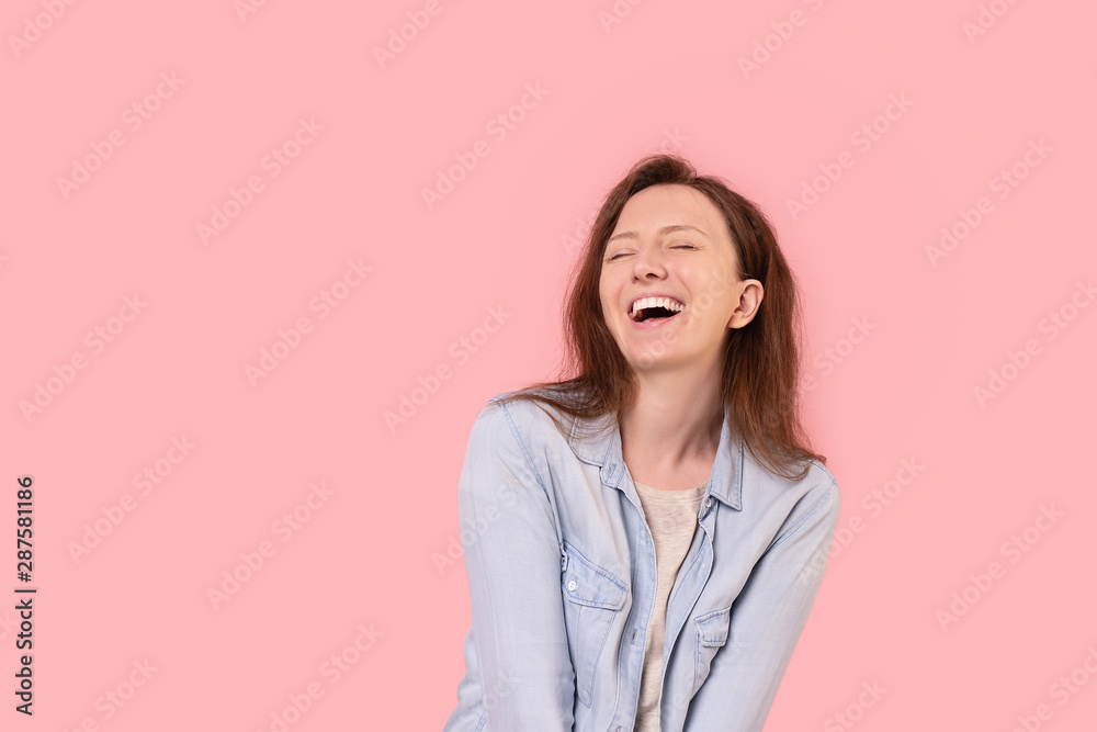 Laughing cheerful positive young woman in casual wear posing on a pink background. Happy young millennial girl rejoices at discounts and promotions in the store. Advertising space Laughing cheerful positive young woman in casual wear posing on a pink background. Happy young millennial girl rejoices at discounts and promotions in the store. Advertising space