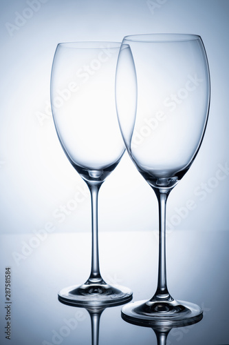 Two glass goblet without wine on a thin leg stands on a mirror surface.