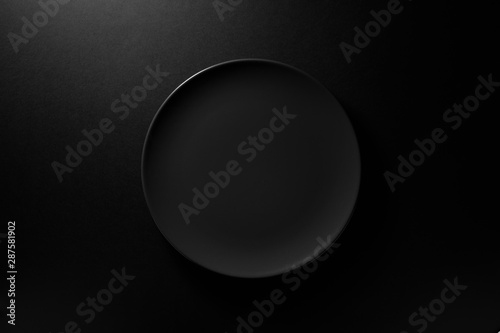 Empty round black plate on dark moody black background with copy space. Overhead view