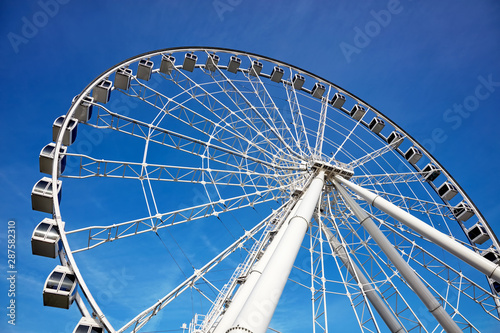 Ferris wheel on blue sky background in amusement park. Majestic view from below