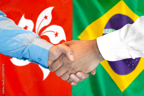 Handshake on Hong Kong and Brazil flag background.