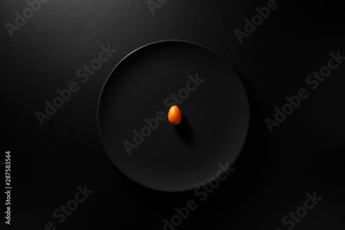 One kumquat served in black plate on moody black background. Top view. Healthy diet concept.