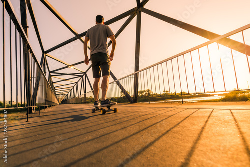 Young skateboarder on bridge at sunset