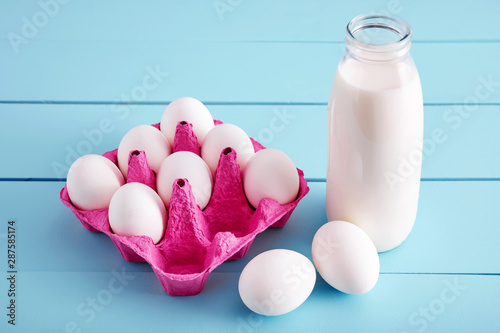 Bottle of milk and white eggs in a pink filler tray on turquoise wooden country kitchen table. Close up ciew from above photo