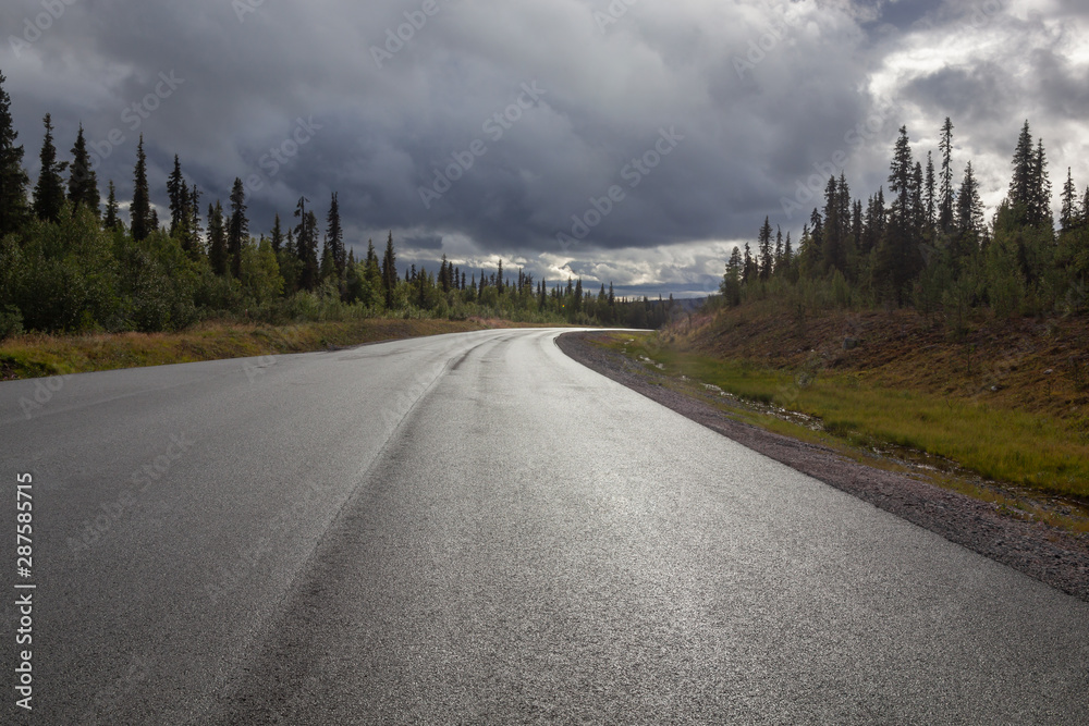 Road across Swedish Lapland is lit with ray of sunlight from under a thundercloud