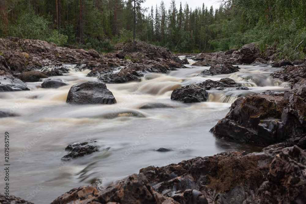 The turbulent river flows on stones in the forest, Northern Swedish. Blurred water on the slow shutter-speed The turbulent river flows on stones in the forest, Northern Swedish. Blurred water on the slow shutter-speed