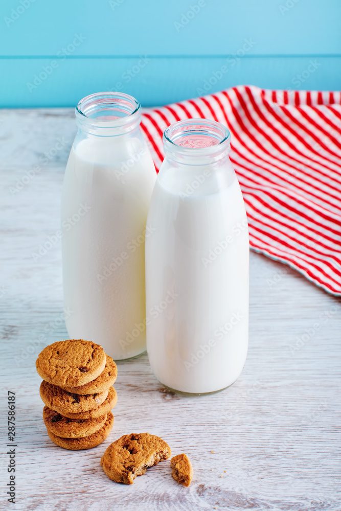 Two bottles of milk and chocolate chip cookies on wooden table with blue wooden background. Two bottles of milk and chocolate chip cookies on wooden table with blue wooden background.