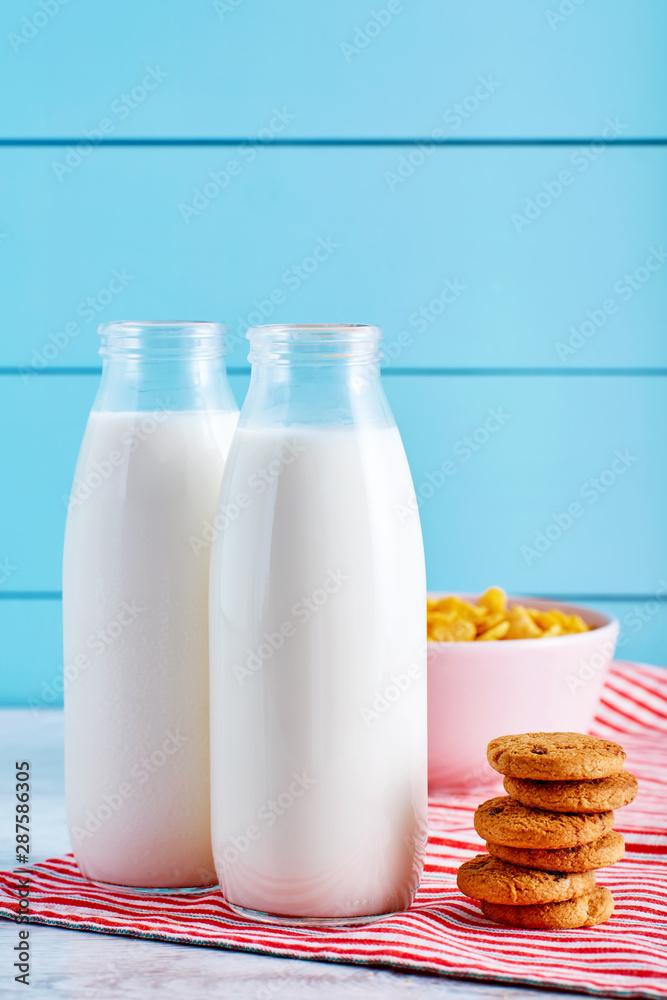 Milk bottles, chocolate chip cookies and a bowl of cereal on wooden table with turquoise wooden background Milk bottles, chocolate chip cookies and a bowl of cereal on wooden table with turquoise wooden background