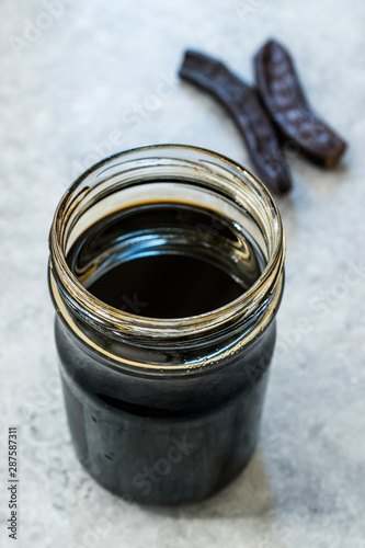 Carob Molasses in Jar with Pods Copy Space. photo