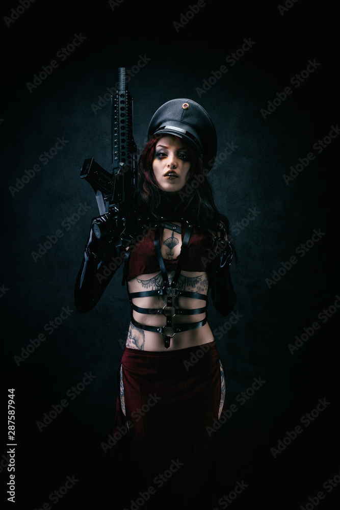 Young black-eyed Cyborg in leather armor and a cap holding a machine gun in his hands Young black-eyed Cyborg in leather armor and a cap holding a machine gun in his hands