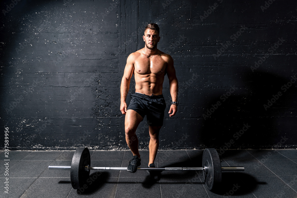 Young muscular sweaty man with big muscles standing above heavy barbell weight after training workout in the gym dark image real people Young muscular sweaty man with big muscles standing above heavy barbell weight after training workout in the gym dark image real people