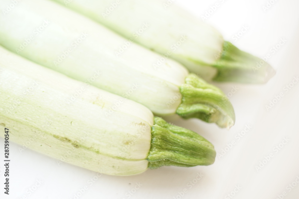 Three fresh vegetable marrow lies on white table. Closeup, diagonal view. Three fresh vegetable marrow lies on white table. Closeup, diagonal view.