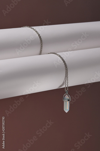 Close-up shot of a steely chainlet with a pendant in the form of screw with a fitted-in bluish gemstone similar to a moonstone. The stone is elongated, conical and has specific inner radiance. 