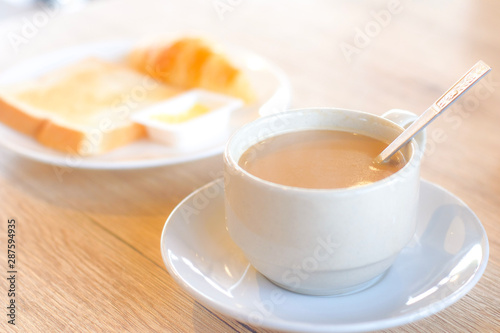 Fresh delicious breakfast with hot coffee in white cup and blur crispy toasts on wooden table.