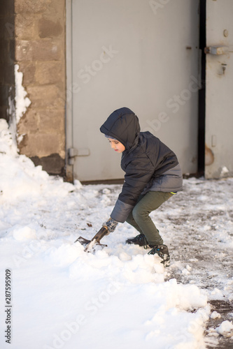 Winter portrait of a child near the garage working with a shovel. Snow drifts, snowstorm. © vik_li
