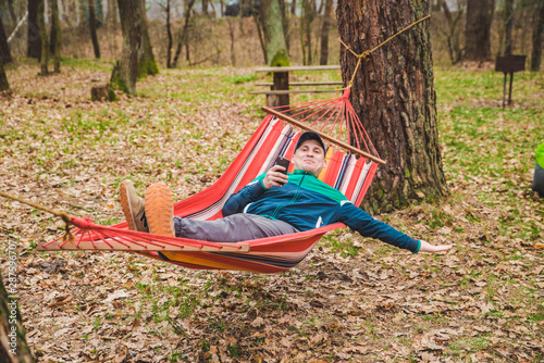 young man laying in hammock surfing in phone