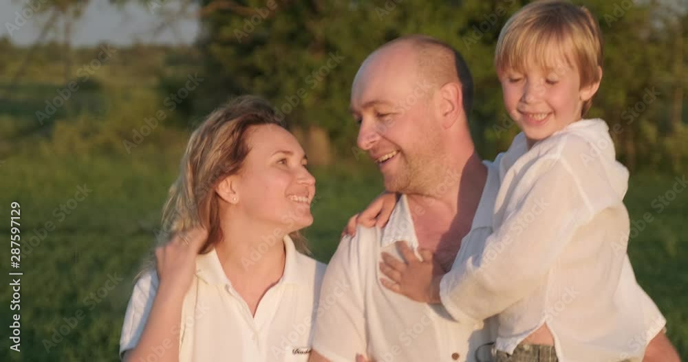 Happy family with child walks on the meadow in the summer. Mother, father and 7 year old son strolls on the field. Happiness. Adult parents with blond boy sauntering in nature. Slow motion. Happy family with child walks on the meadow in the summer. Mother, father and 7 year old son strolls on the field. Happiness. Adult parents with blond boy sauntering in nature. Slow motion.