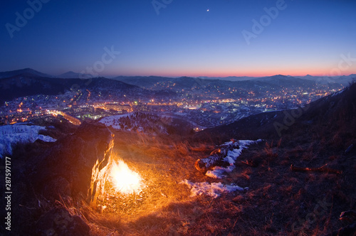 Night fire on the mountain on the background of the town village under a sunset sky