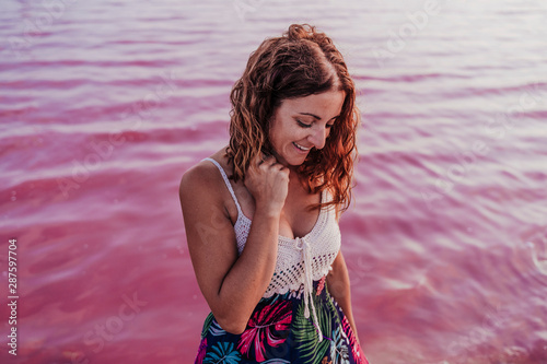 portrait of young beautiful woman standing by a pink lake or lagoon in a natural park at sunset. Torrevieja, Spain.Tourism and travel concept