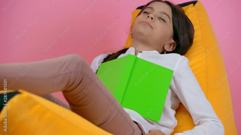 child sleeping with book on bean bag chair isolated on pink