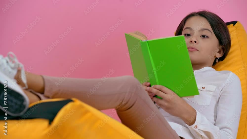 emotional child reading book on bean bag chair isolated on pink emotional child reading book on bean bag chair isolated on pink