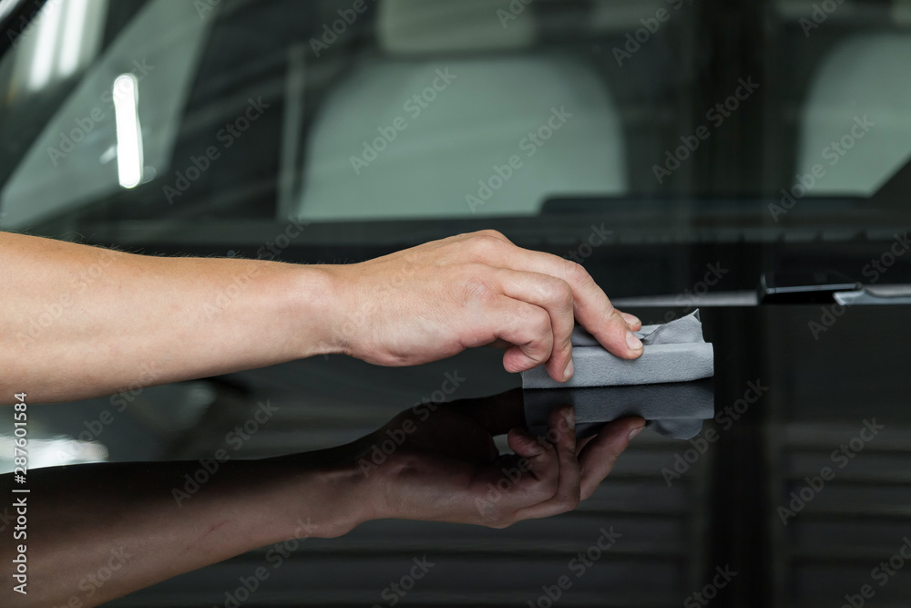 Obraz premium The process of applying a nano-ceramic coating on the car's hood by a male worker with a sponge and special chemical composition to protect the paint on the body from scratches, chips and damage.
