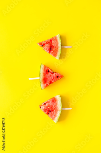Slices of watermelon popsicle on yellow background top view