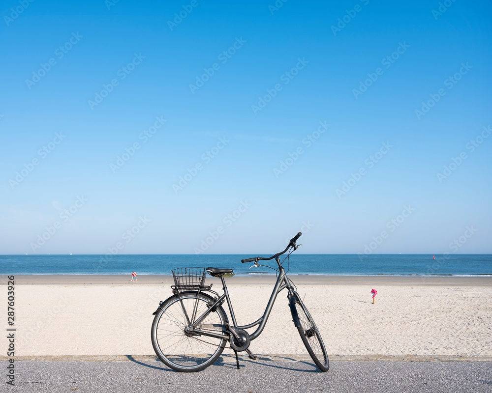 Obraz premium lonely bicycle near large sandy beach of german island norderney off the coast of ostfriesland under blue august sky in summer