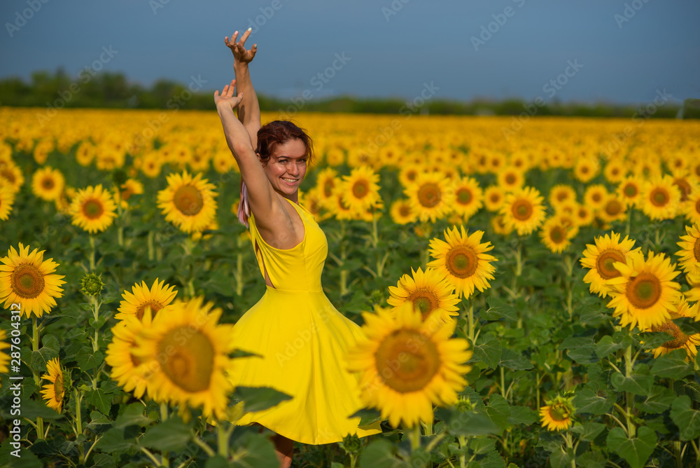Red-haired woman in a yellow dress dancing with raised hands in a field of sunflowers. Beautiful girl in a skirt sun enjoys a cloudless day in the countryside. Pink locks of hair. Red-haired woman in a yellow dress dancing with raised hands in a field of sunflowers. Beautiful girl in a skirt sun enjoys a cloudless day in the countryside. Pink locks of hair.