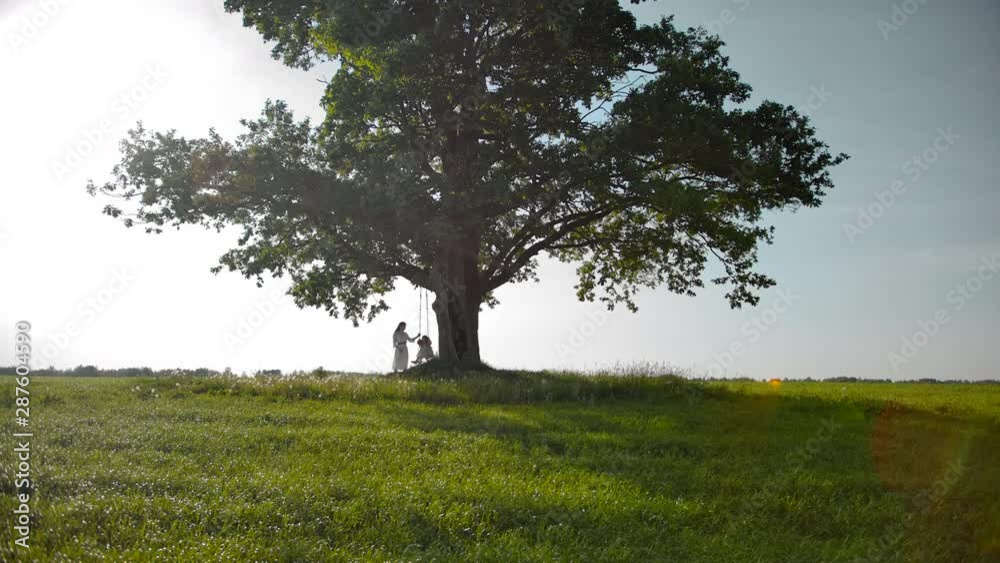 Little silhouettes of family swinging on a swing on a branch of vintage green oak tree. Little silhouettes of family swinging on a swing on a branch of vintage green oak tree.