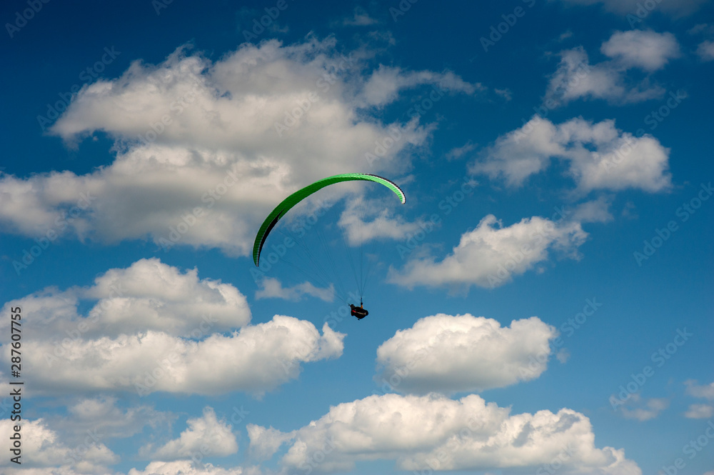 Alone paraglider flying in the blue sky against the background of clouds. Paragliding in the sky on a sunny day. Alone paraglider flying in the blue sky against the background of clouds. Paragliding in the sky on a sunny day.