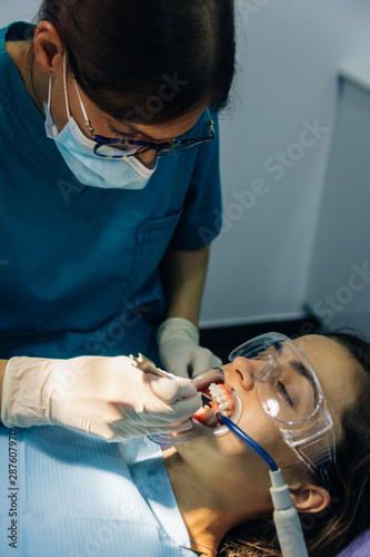 Canvastavla process of placing white dental braces to a Caucasian girl in a dental clinic wi