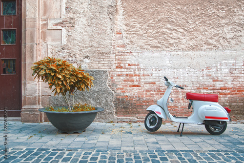 Fototapeta Naklejka Na Ścianę i Meble -  Vintage scene with a scooter motorcicle in a small town in Italy parked in front of a church facade. Empty copy space for Editor's text.