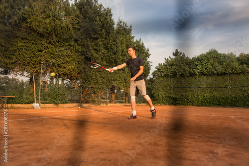 Young man playing and enjoying tennis on the clay court during lovely summer day © Khaligo