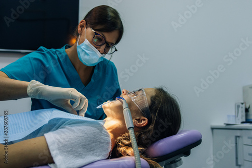 process of placing white dental braces to a Caucasian girl in a dental clinic with a dentist girl