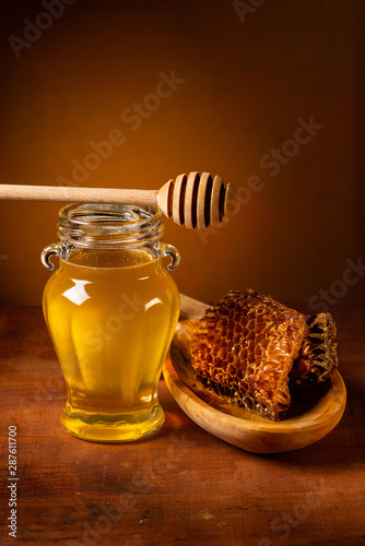 still life: on the rough wooden floor, glass vase with acacia honey, wooden ladle and honeycomb photo