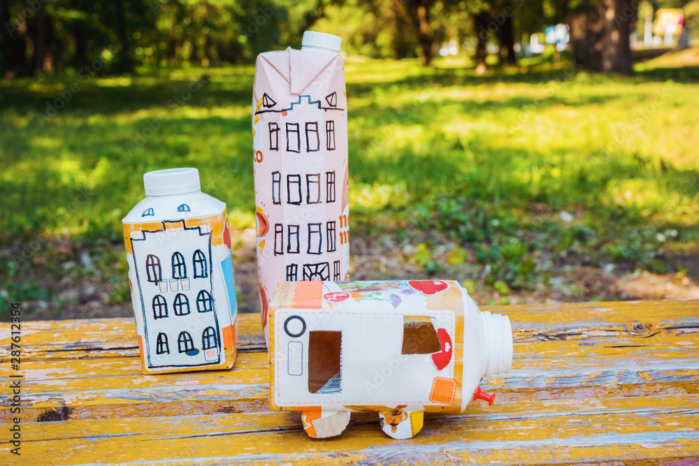 Houses and toy cars made from milk bags on grass. DIY paper milk bag. Creative paper milk bag ideas. Recycle crafts.