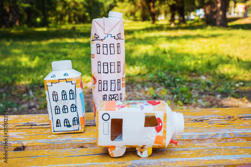 Obraz na płótnie Houses and toy cars made from milk bags on grass. DIY paper milk bag. Creative paper milk bag ideas. Recycle crafts. w salonie